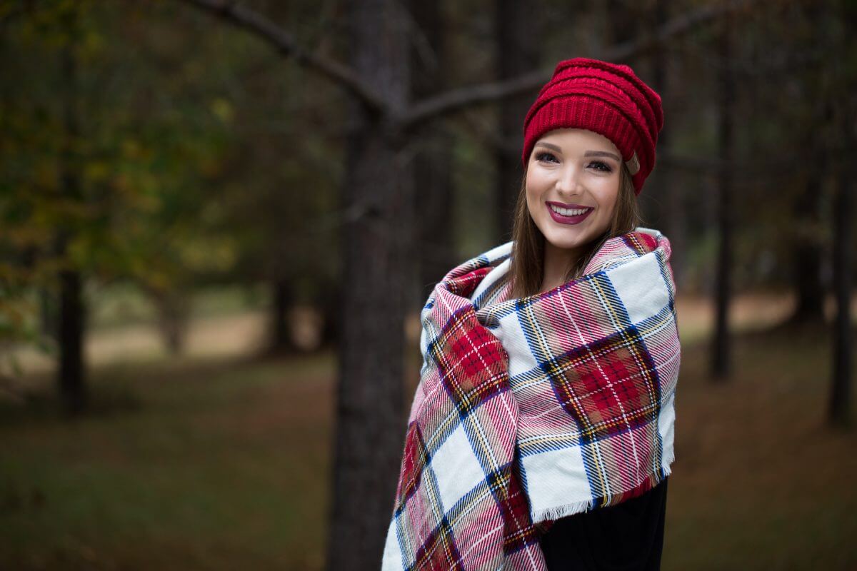 brunette high school senior in red beanie and red plaid shawl in wooded area