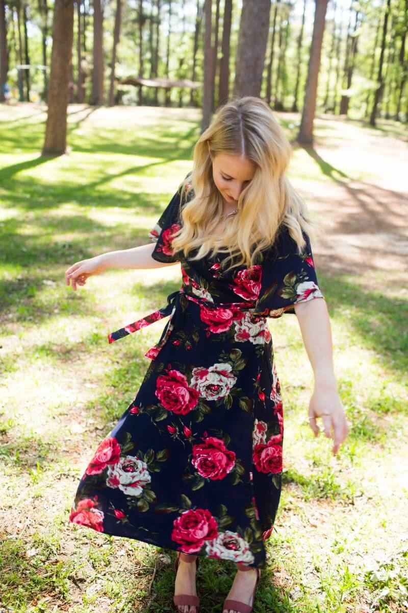 Blonde woman twirling in blue and red floral dress in wooded park
