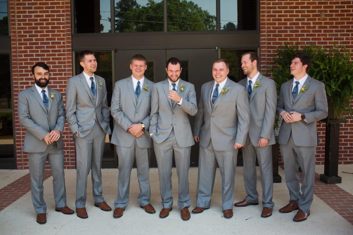 groom and groomsmen laughing and posing in front of red brick church