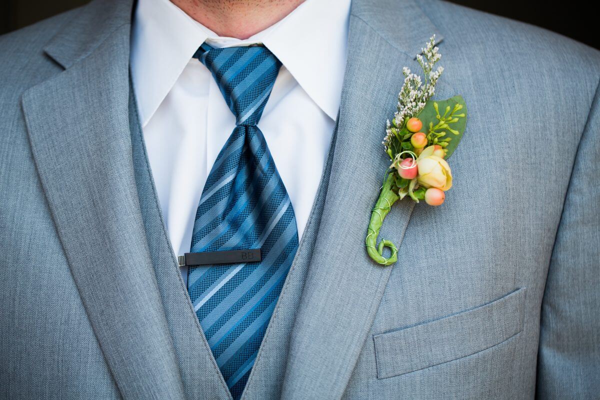 detail shot of groom's blue tie and black tie pin and small rose corsage