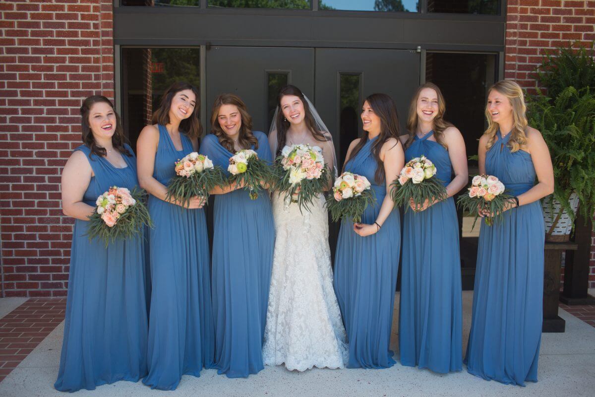 bride and bridesmaids laughing and posing in front of red brick church