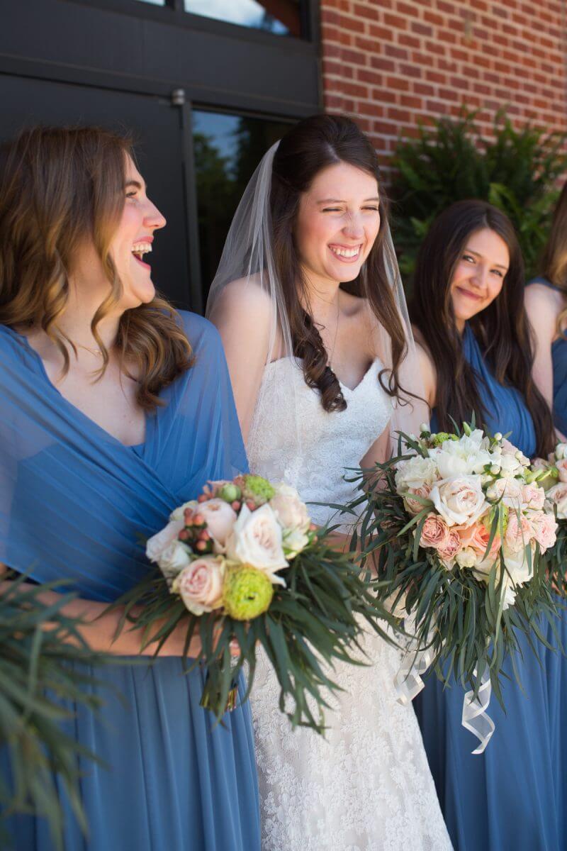 bride with bouquet laughing with brides maids in blue dresses