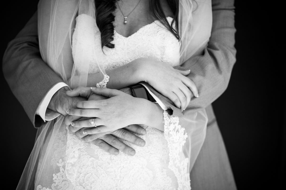 detail of bride and groom's hands as groom hugs bride from behind