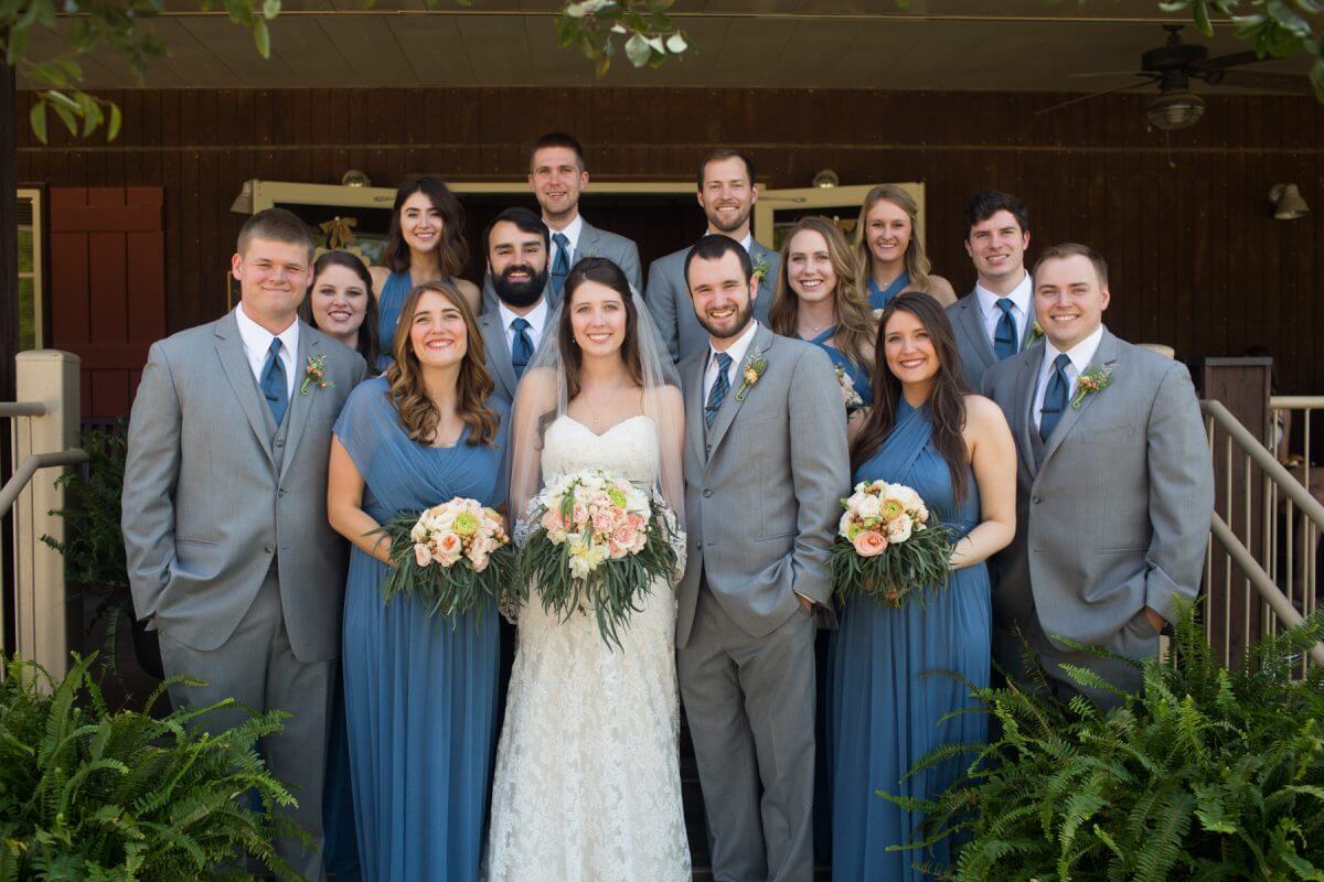 bridal party with bride and groom and groomsmen in gray suits and bridesmaids in blue dresses
