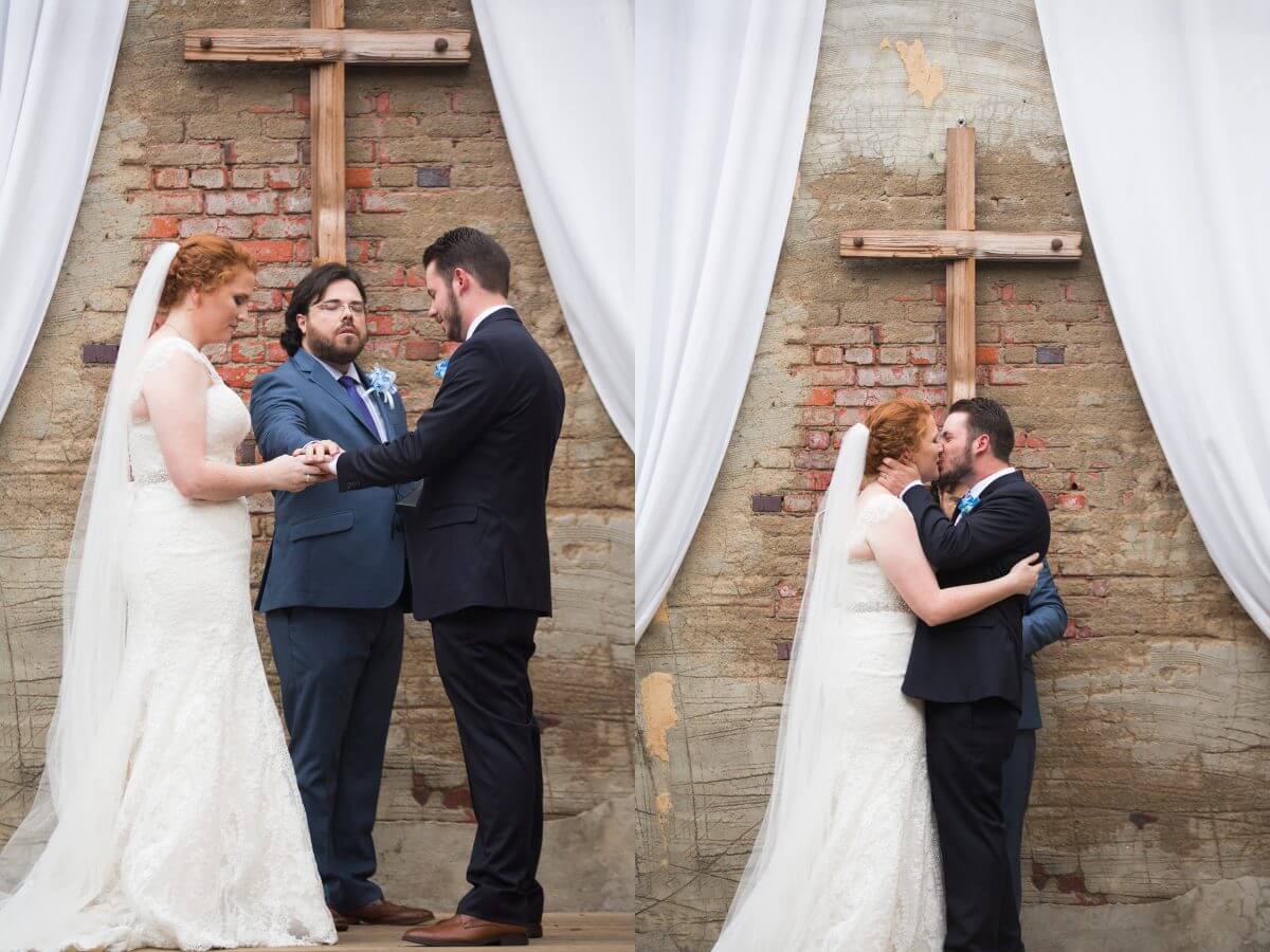 bride and groom with officiant in front of cross and kissing in front of cross