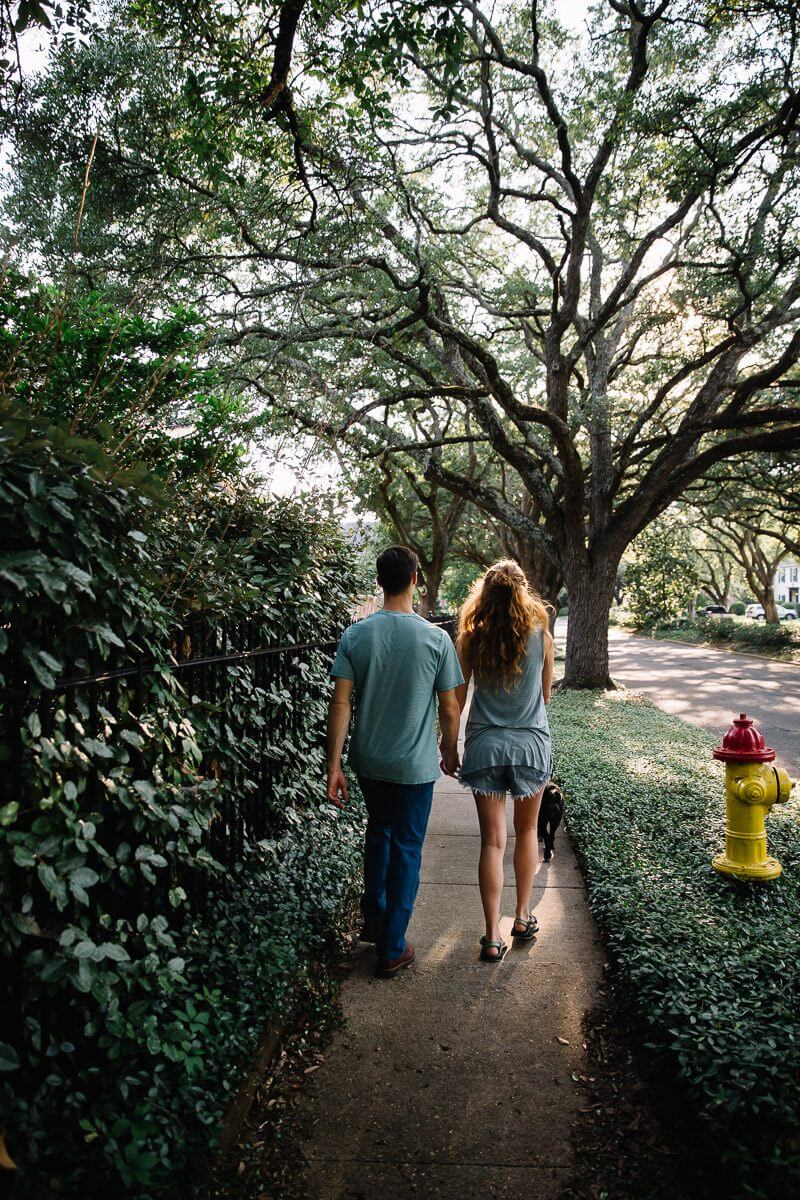 couple holding hands and walking their dog down oak lined street in Shreveport, Louisiana during an at home engagement session